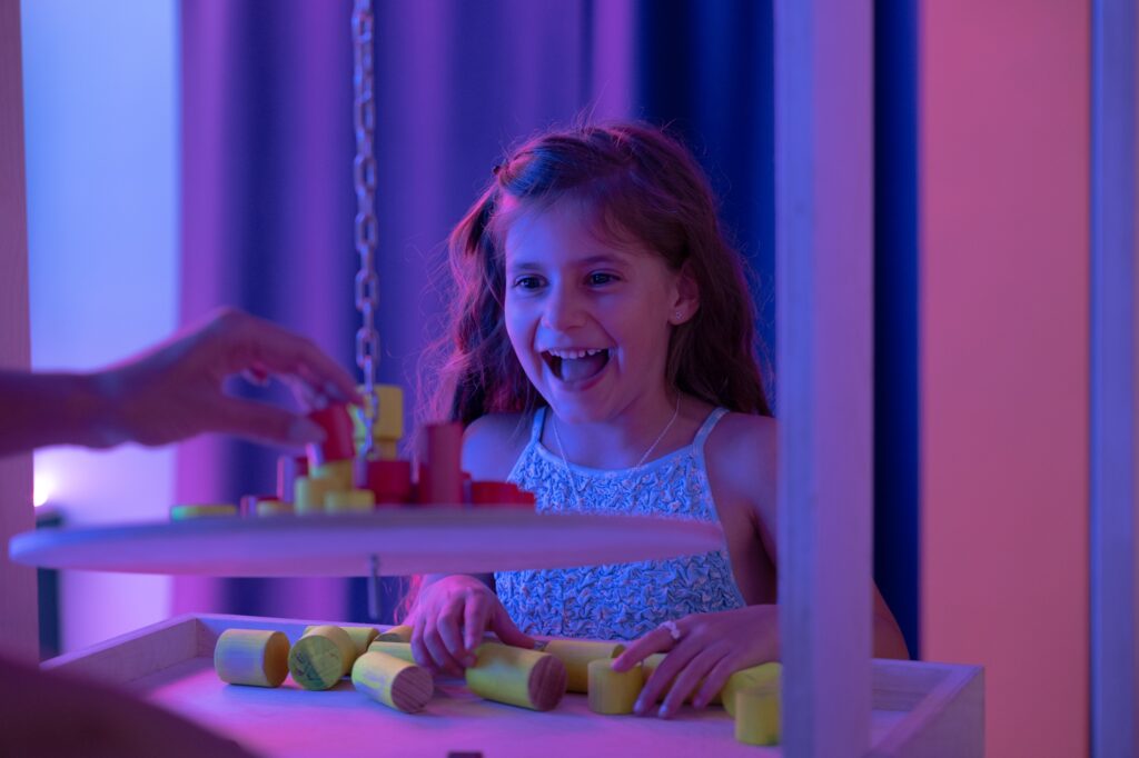 Criança a sorrir enquanto brinca com blocos coloridos numa instalação interativa do museu Neonia Porto.